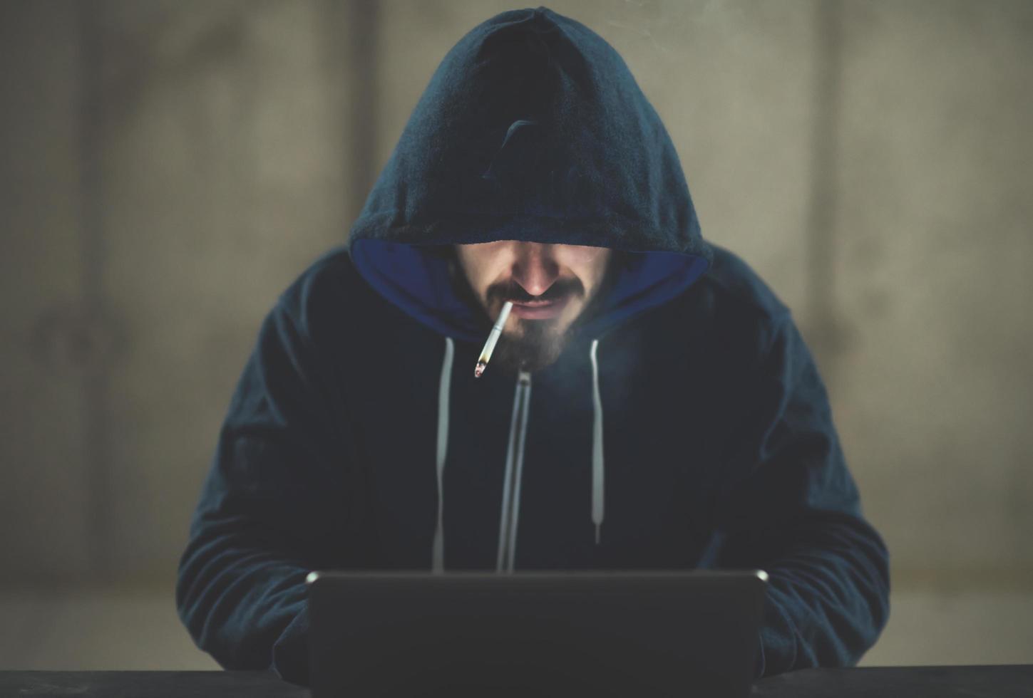 jeune hacker utilisant un ordinateur portable tout en travaillant dans un bureau sombre photo