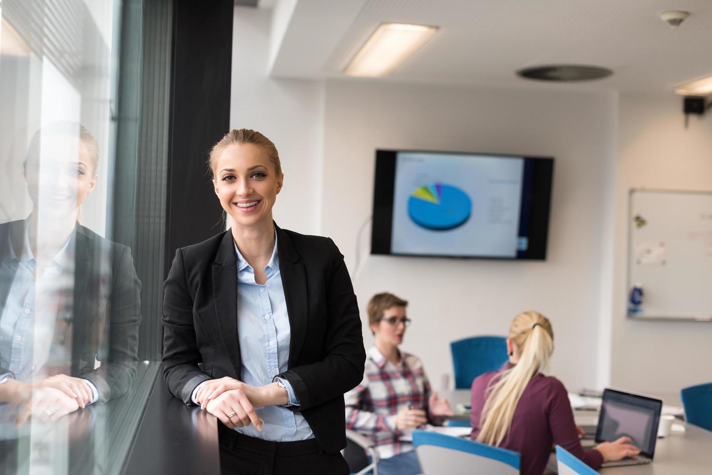 portrait d'une jeune femme d'affaires au bureau avec une équipe lors d'une réunion en arrière-plan photo