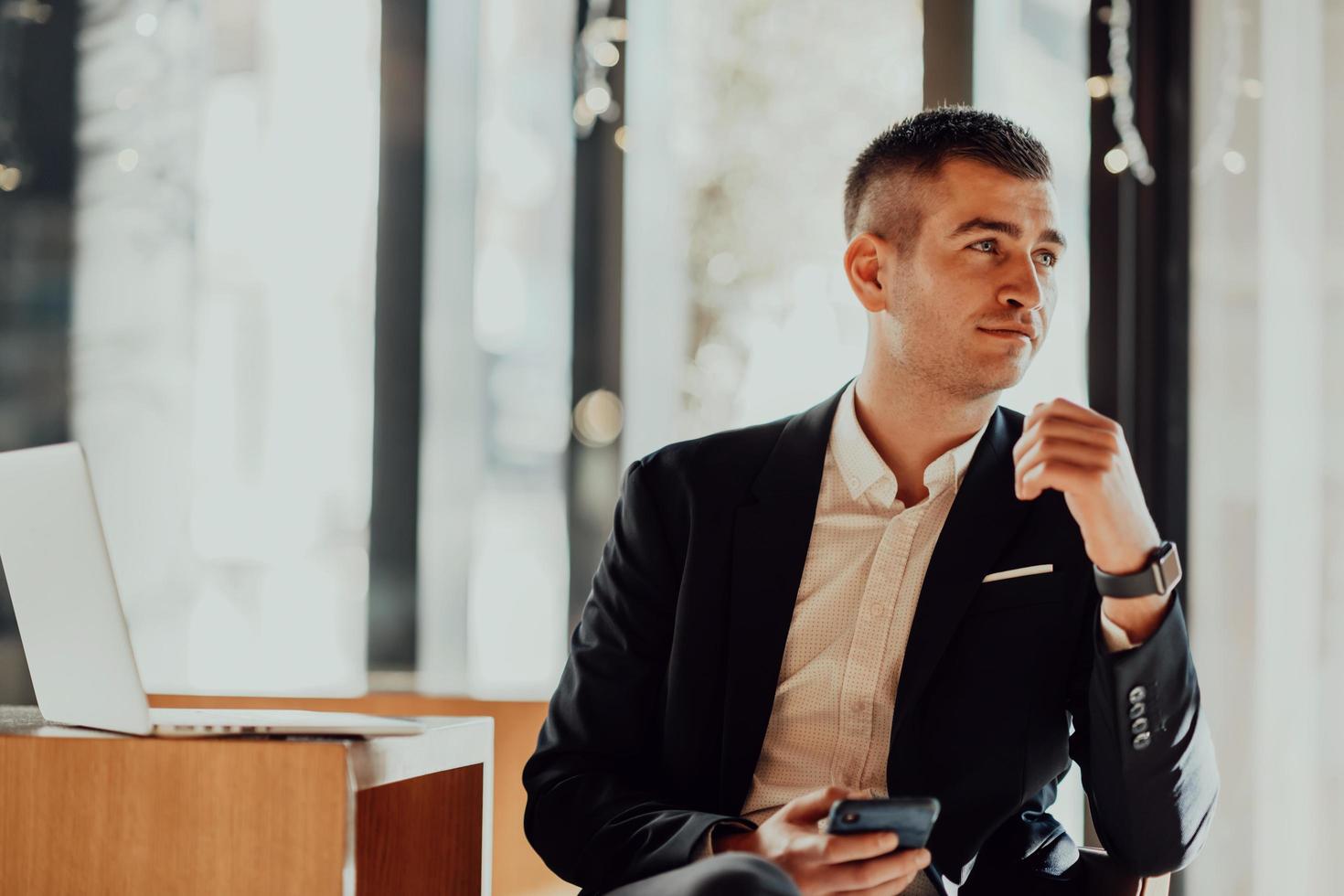 homme d'affaires heureux assis à la cafétéria avec ordinateur portable et smartphone photo