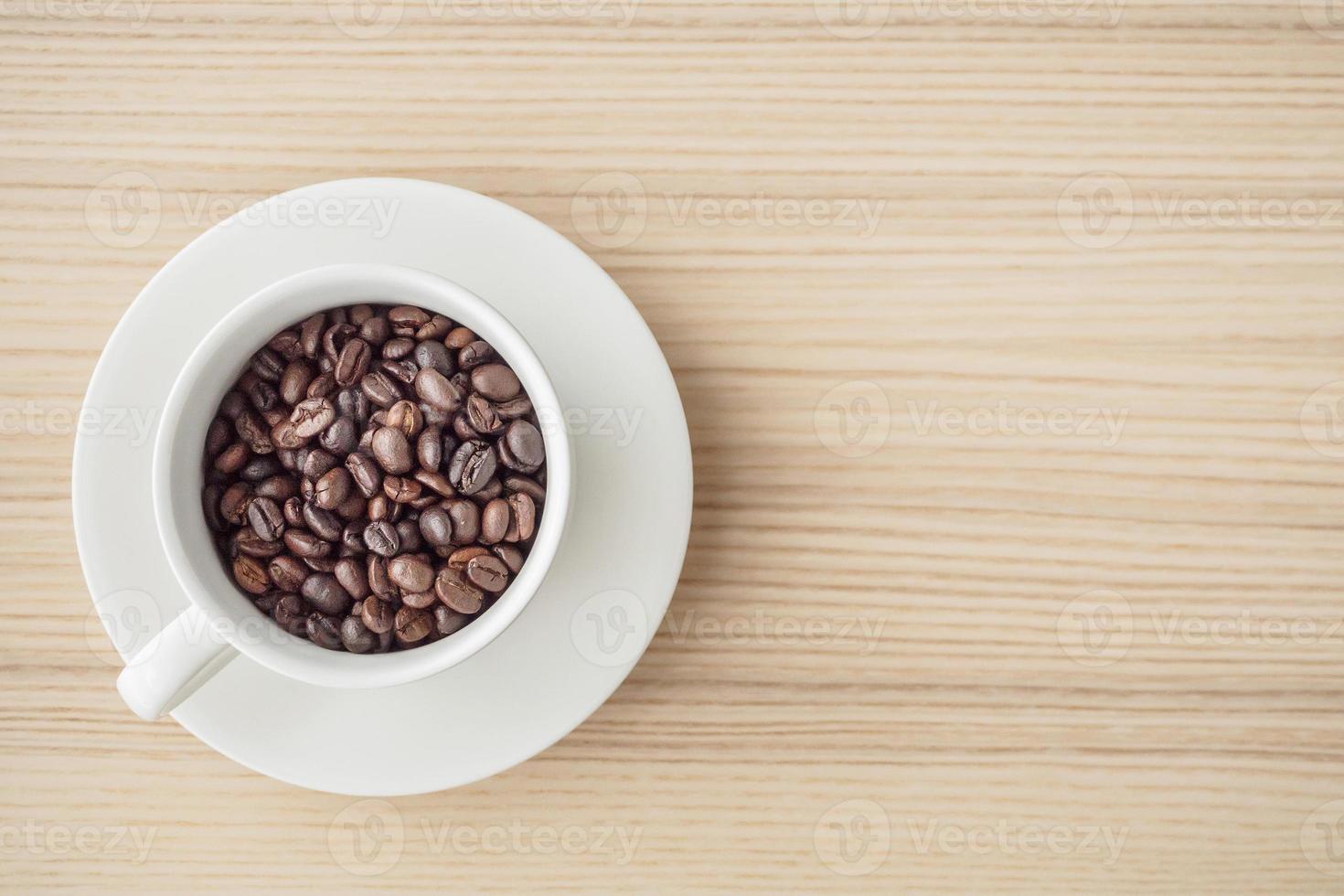 grains de café torréfiés frais dans une tasse blanche sur une table en bois, vue de dessus photo