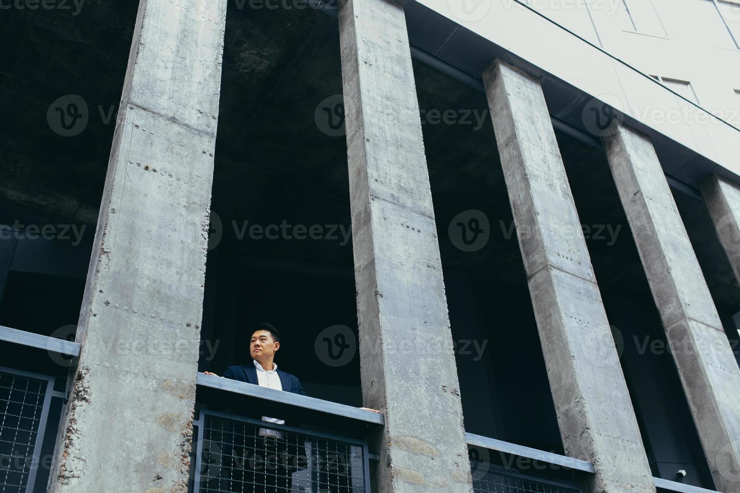 jeune homme d'affaires asiatique debout près d'un immeuble de bureaux noir moderne en béton photo