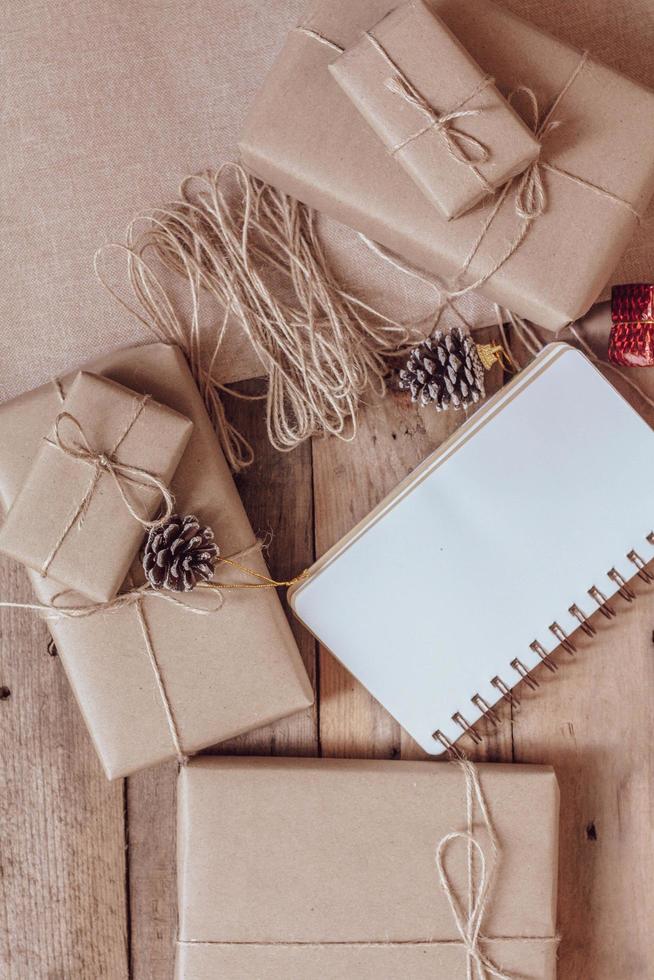 boîte-cadeau de noël utiliser du papier recyclé brun et un cahier et des pommes de pin sur une table en bois. photo