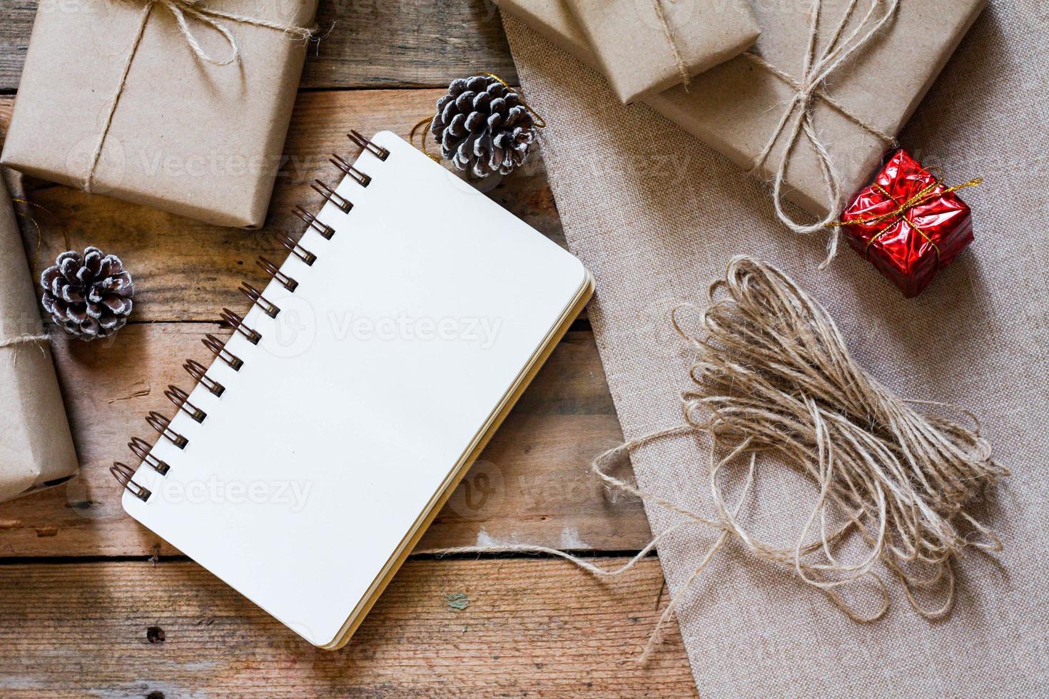 boîte-cadeau de noël utiliser du papier recyclé brun et un cahier et des pommes de pin sur une table en bois. photo