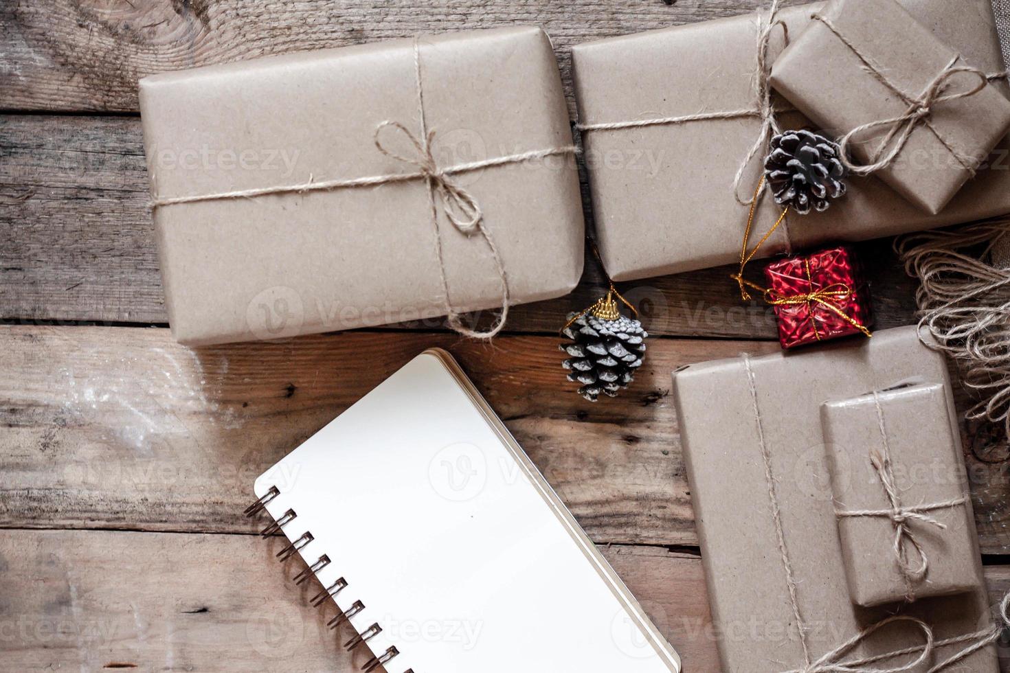 boîte-cadeau de noël utiliser du papier recyclé brun et un cahier et des pommes de pin sur une table en bois. photo