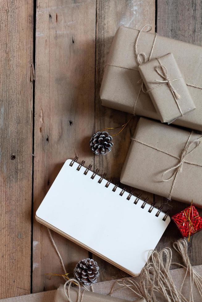 boîte-cadeau de noël utiliser du papier recyclé brun et un cahier et des pommes de pin sur une table en bois. photo