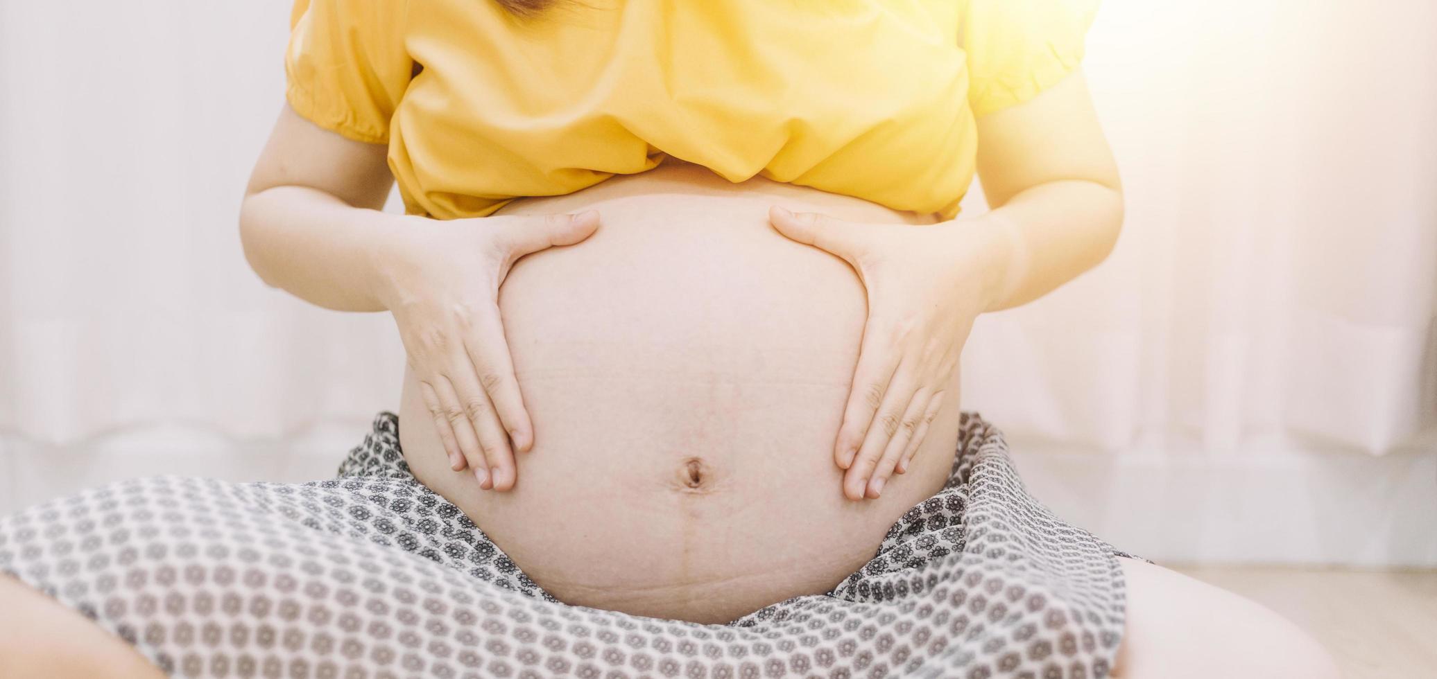 jeune femme enceinte adulte en vêtements blancs touchant un gros ventre nu avec les mains. montrant la forme. notion de grossesse. temps d'attente. fermer. isolé sur fond de mur gris clair. photo