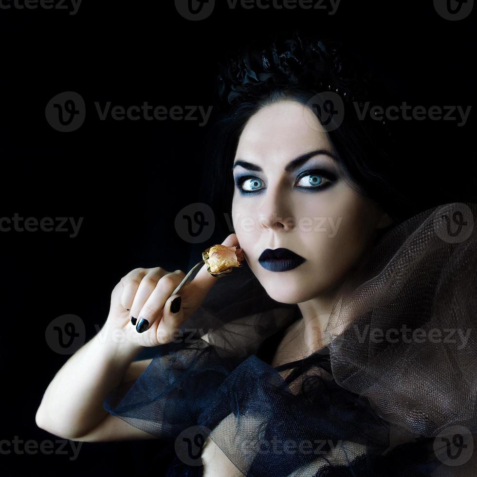 femme gothique aux cheveux noirs avec des lèvres noires maquillage et rose sèche dans sa main photo