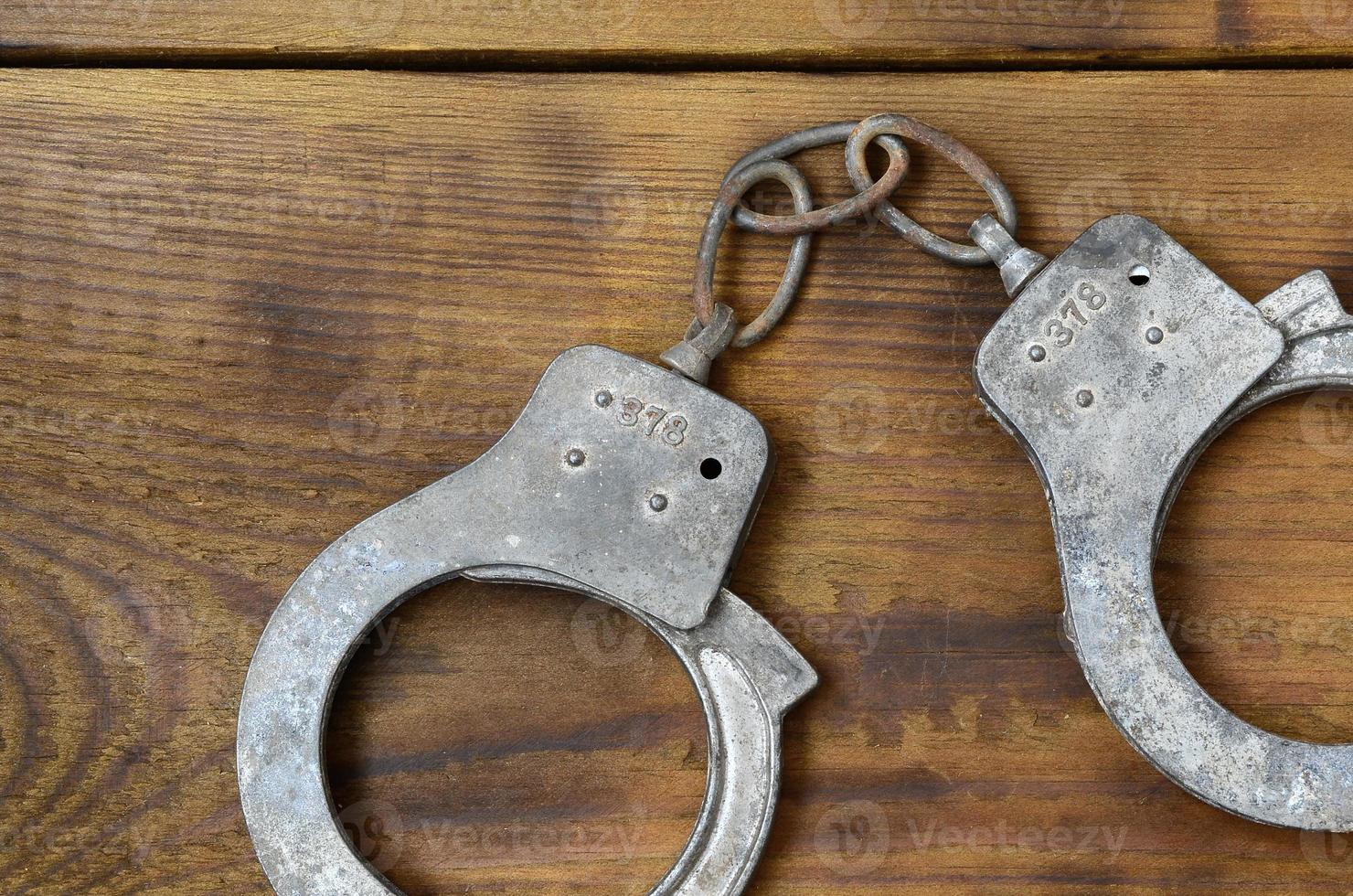 des menottes de police anciennes et rouillées reposent sur une surface en bois rayée. le concept d'un crime ancien photo