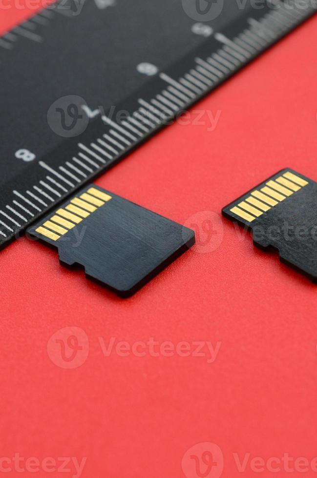 deux petites cartes mémoire micro sd se trouvent sur un fond rouge à côté d'une règle noire. un magasin de données et d'informations petit et compact photo