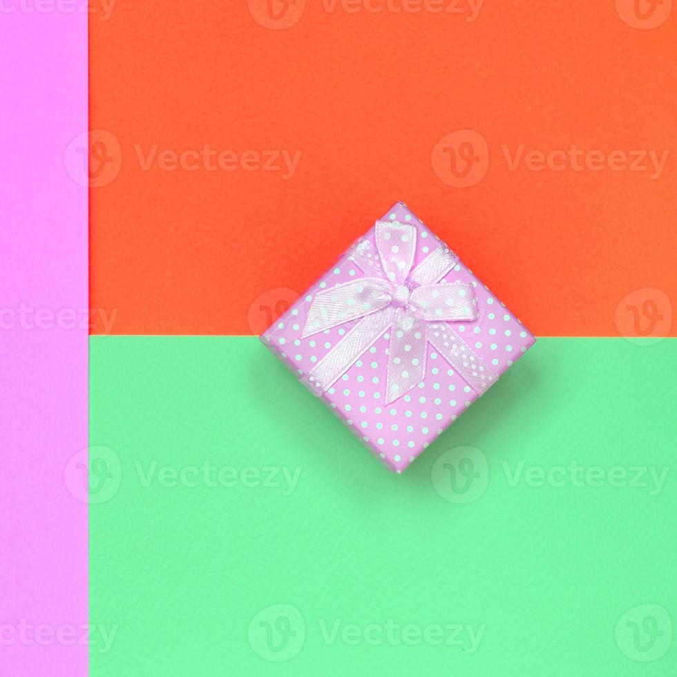petite boîte cadeau rose se trouve sur fond de texture de papier de couleurs pastel turquoise, rouge et rose photo