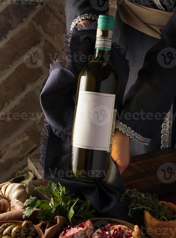 une photo verticale d'une personne en costume traditionnel montrant une bouteille de vin