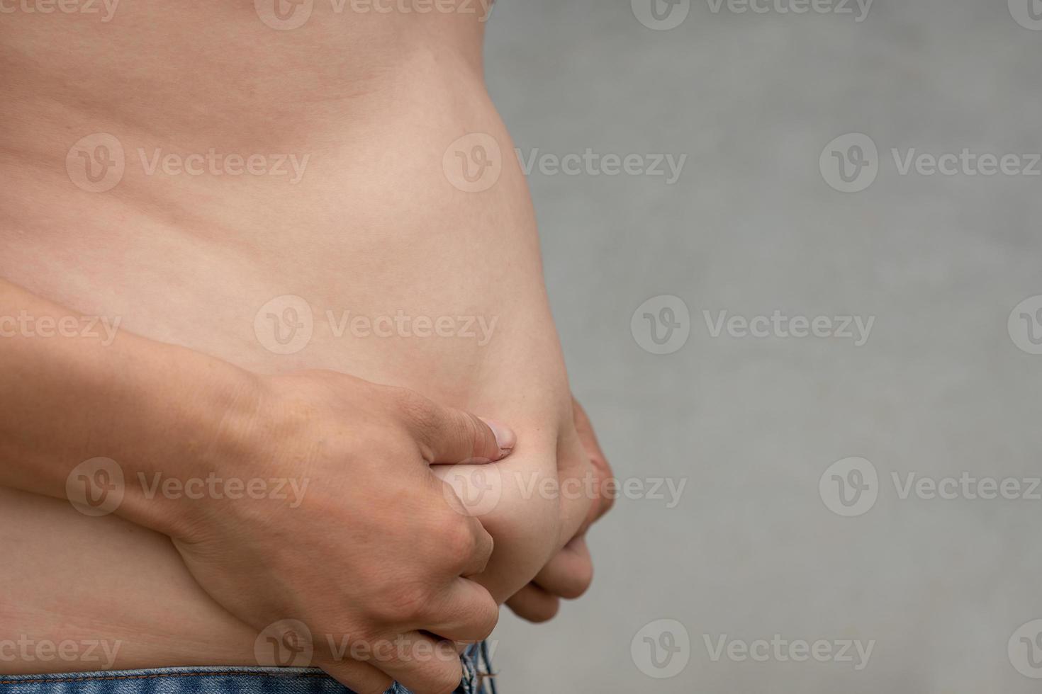 gros plan d'un homme asiatique attrape l'estomac avec un pantalon en jean et un arrière-plan flou de ciment, planifie l'exercice et la perte de poids pour une bonne santé dans l'espace de copie du concept de fonction, de soins de santé et de gym photo