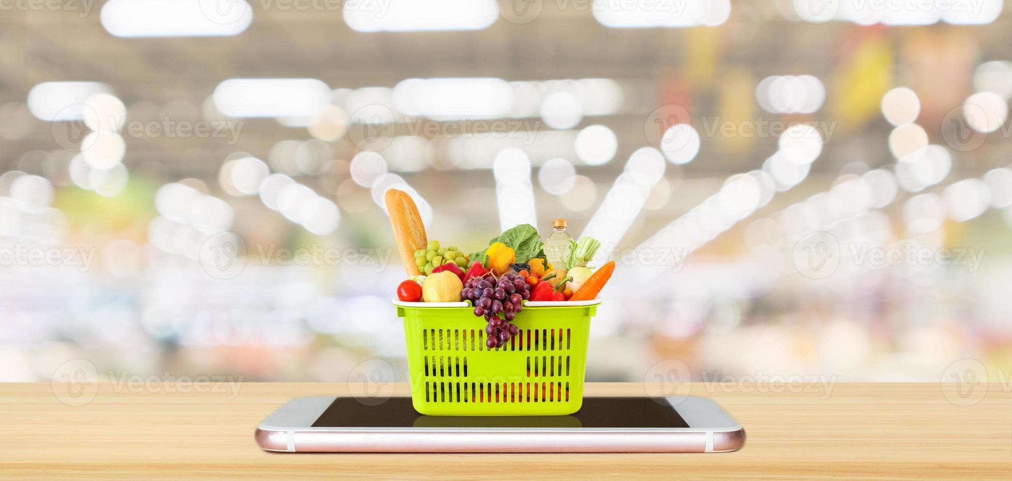 aliments frais et légumes dans le panier sur smartphone mobile sur table en bois avec allée de supermarché arrière-plan flou concept d'épicerie en ligne photo
