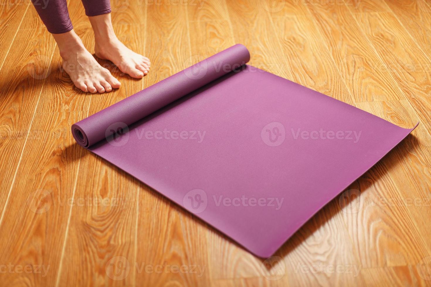 les pieds de la fille se tiennent devant un tapis de yoga déplié sur le parquet. photo