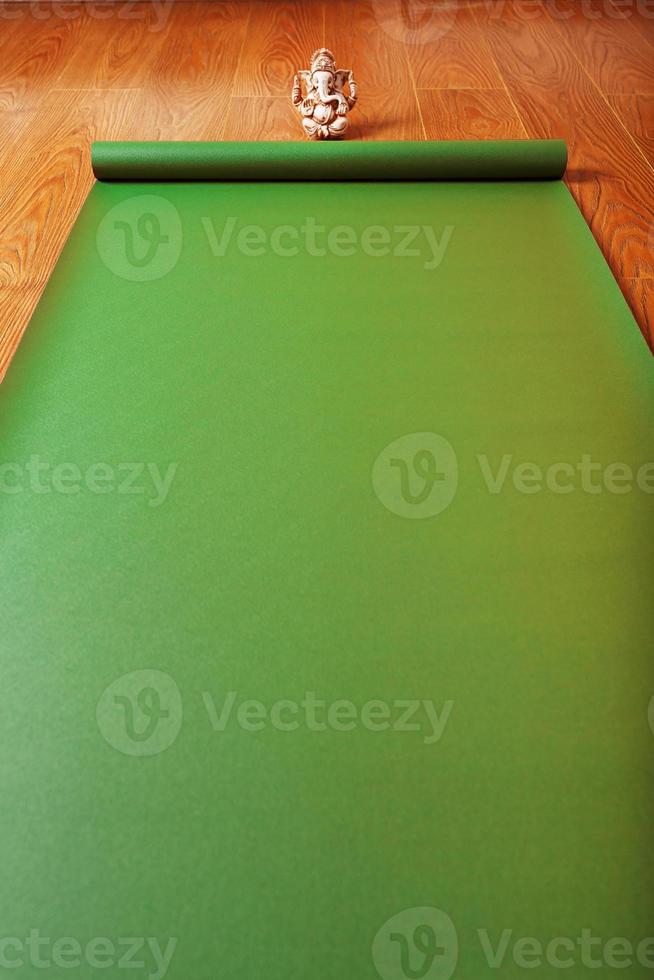un tapis de yoga vert déplié sur le parquet avec une figurine de ganesha. photo