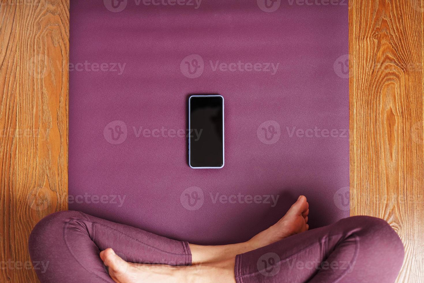 une fille pratiquant le yoga et la méditation à la maison sur un tapis lilas à l'aide d'un smartphone et d'une application mobile. photo