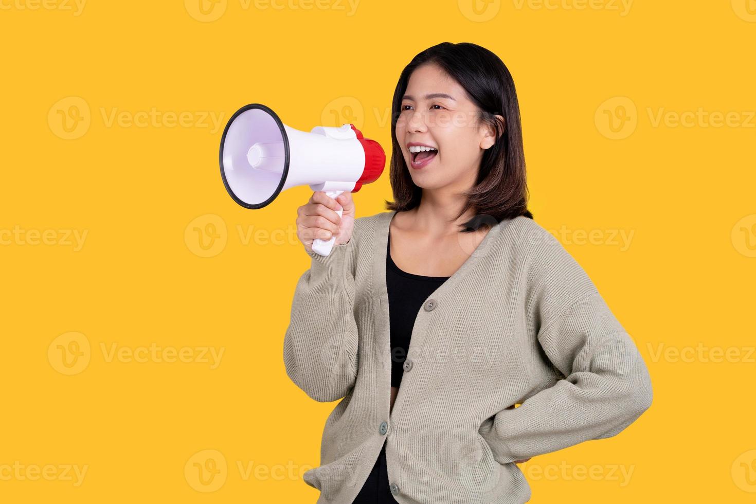 heureuse belle femme asiatique aux cheveux noirs en pull vert isolé sur fond jaune en studio. elle criait dans le mégaphone. photo