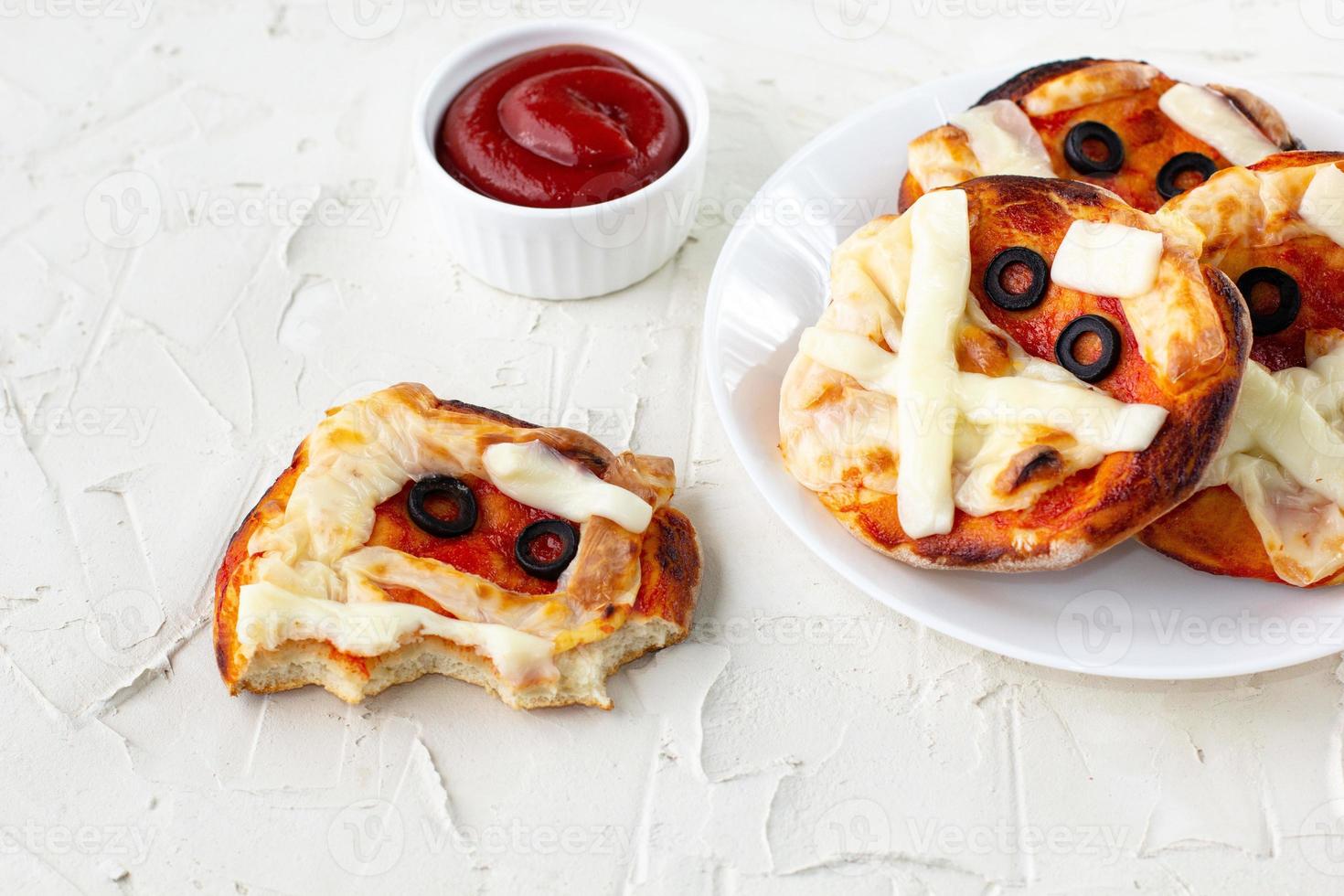 mini pizza comme momie pour les enfants avec du fromage, des olives et du ketchup. drôle de nourriture folle d'halloween pour les enfants photo