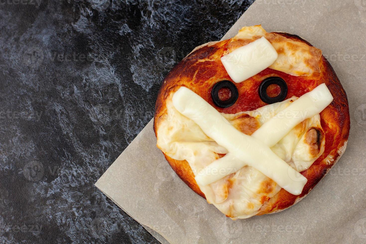 mini pizza comme momie pour les enfants avec du fromage, des olives et du ketchup. drôle de nourriture folle d'halloween pour les enfants. photo