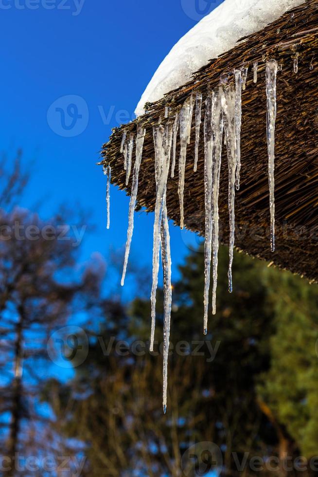 Glaçons sur le coin du toit de la maison en bois photo