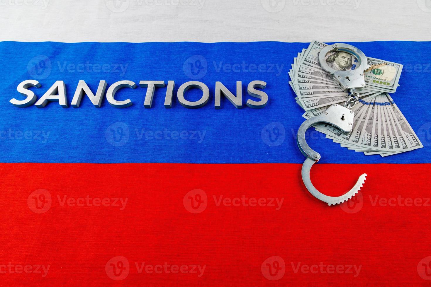 le mot sanctions posées avec des lettres en métal argenté sur le drapeau tricolore russe près des billets en dollars et des menottes en perspective linéaire photo