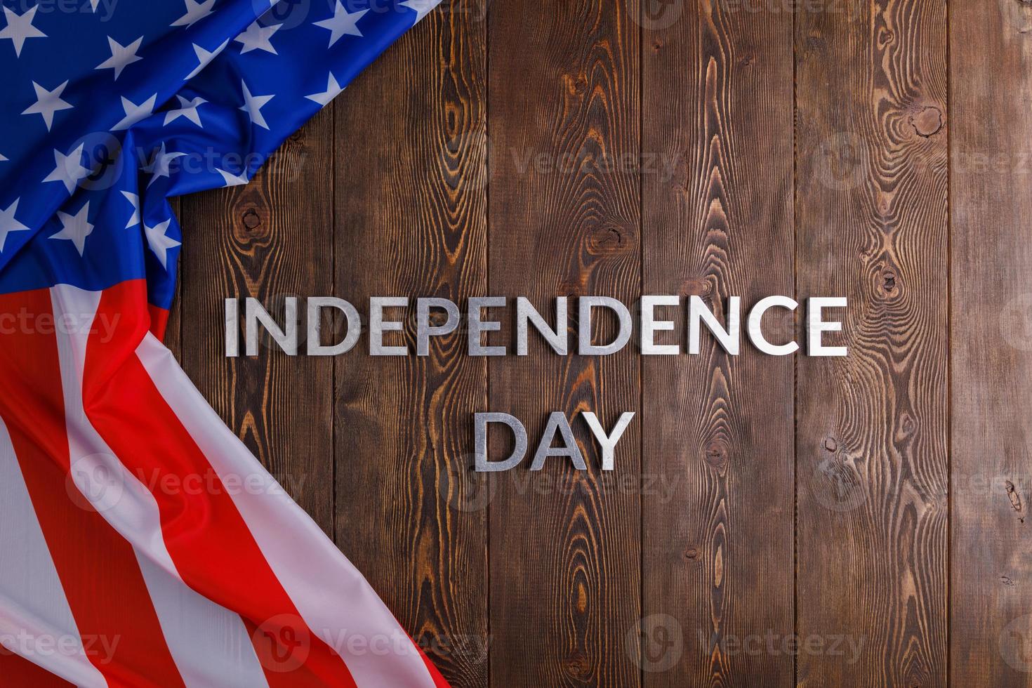 les mots fête de l'indépendance posés sur la surface de planches de bois marron avec le drapeau des états-unis d'amérique froissé photo