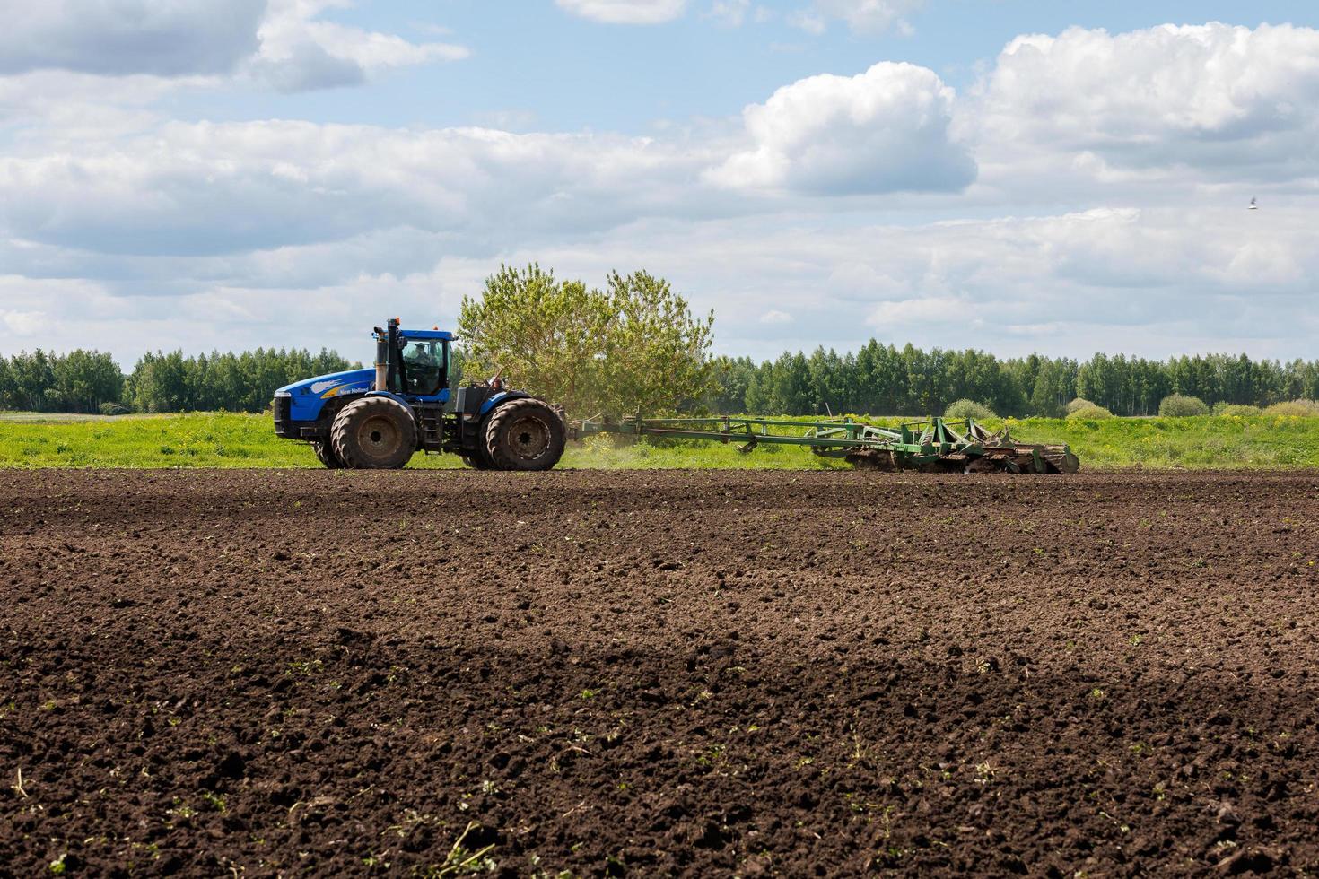 tracteur bleu avec roues doubles tirant une herse à disques avec panier à rouleaux lors d'une chaude journée ensoleillée photo