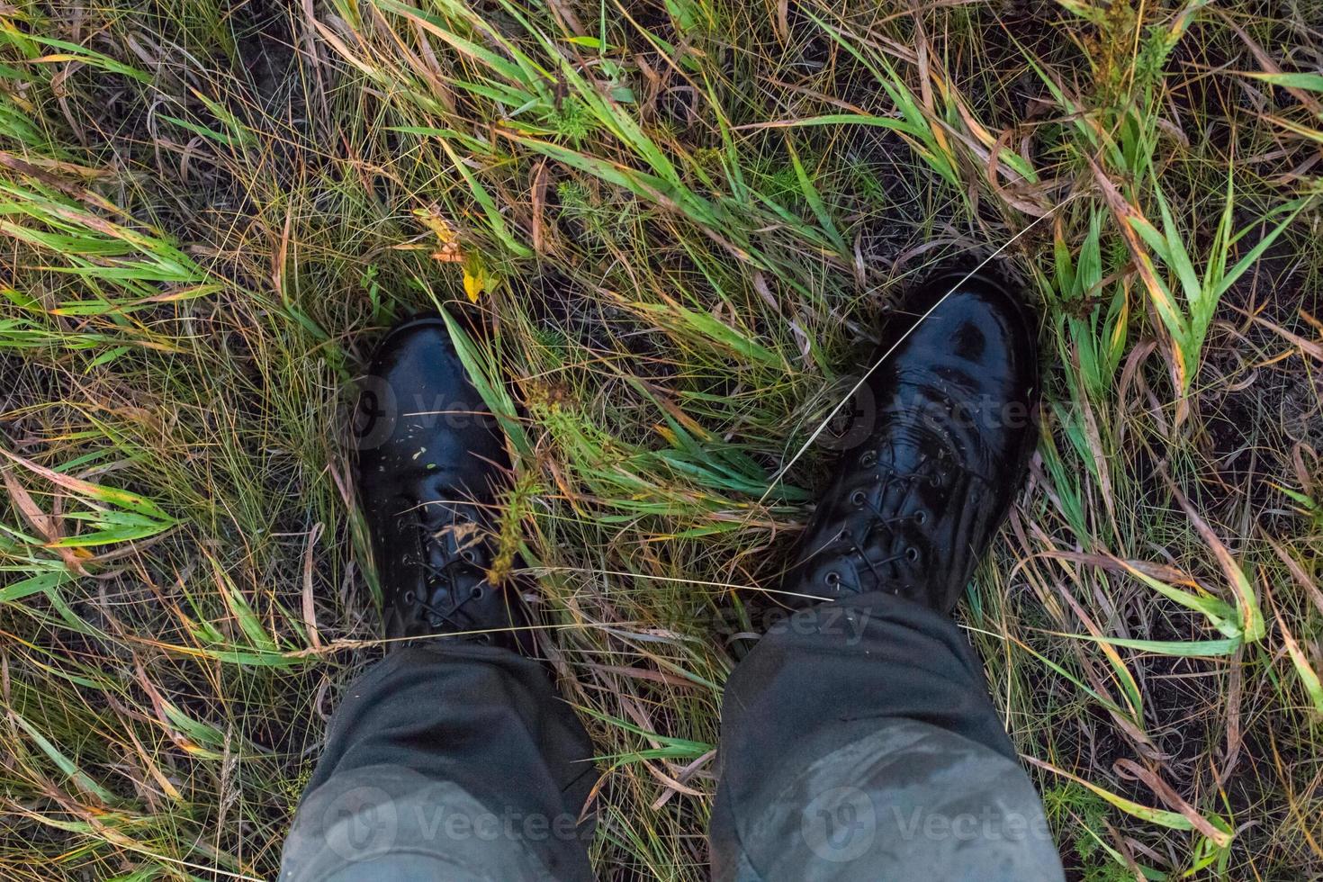 pieds dans des bottes militaires noires mouillées et un pantalon en coton vert dans l'herbe d'automne gonzo point de vue vers le bas. photo