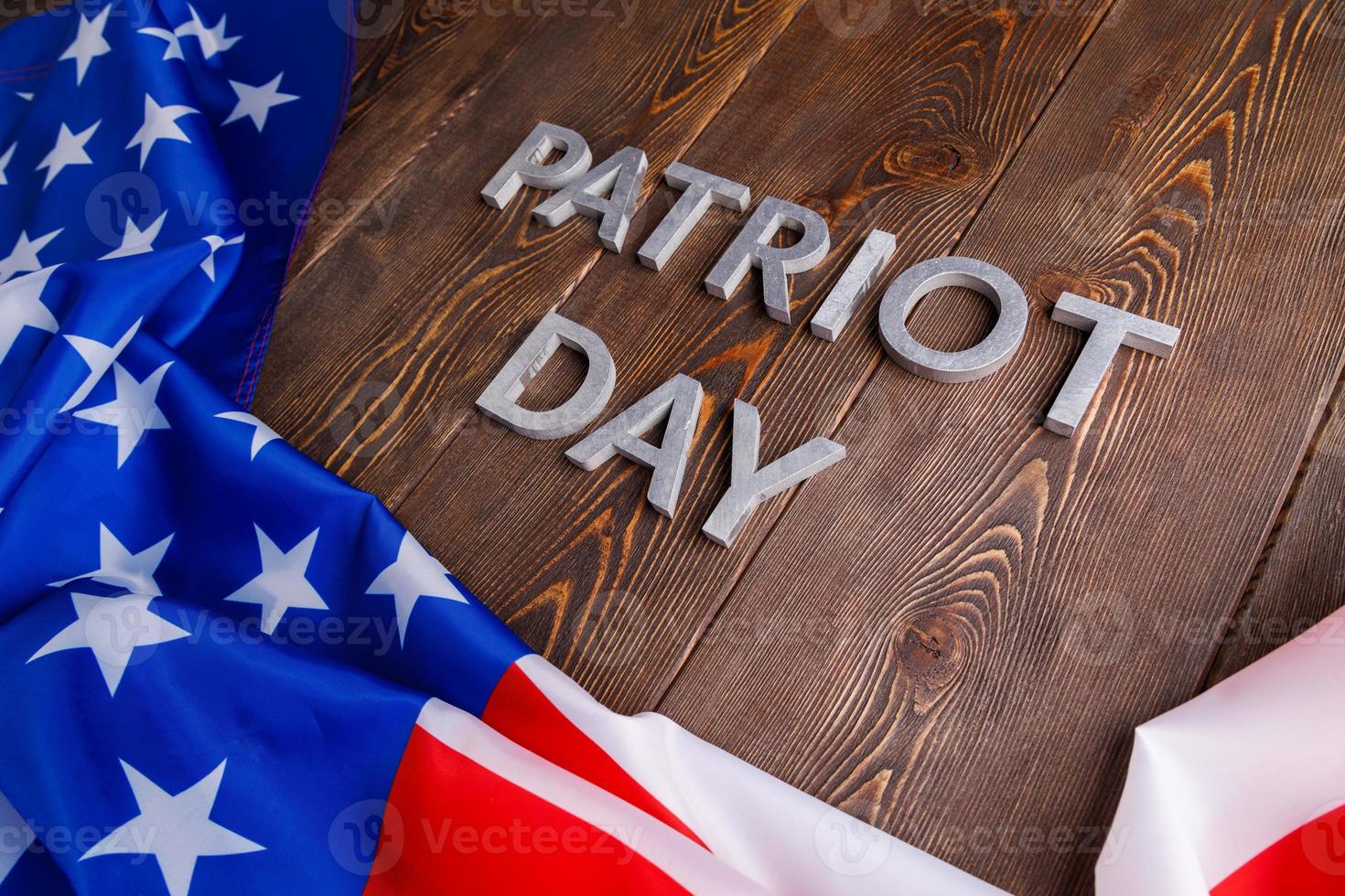 les mots patriot day posés avec des lettres en métal argenté sur la surface de la planche de bois avec le drapeau usa froissé photo