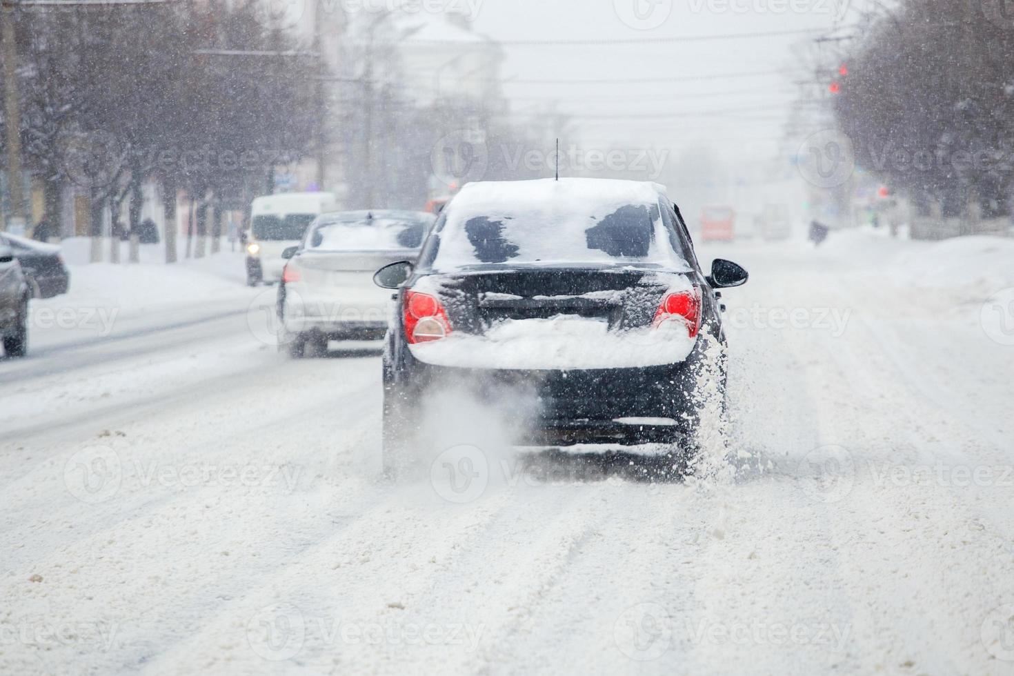la neige de la route s'envole du rouet d'un véhicule. les roues de la  voiture patinent et crachent des morceaux de neige, elle tente de gagner en  traction sur la route glissante.