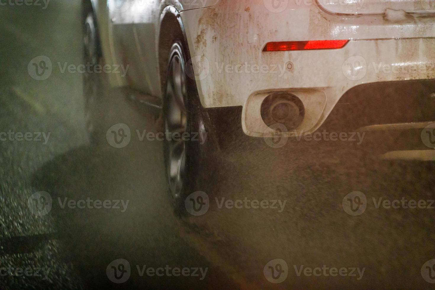 L'eau sale s'éjecte de la voiture blanche roulant sur la route d'hiver de nuit photo