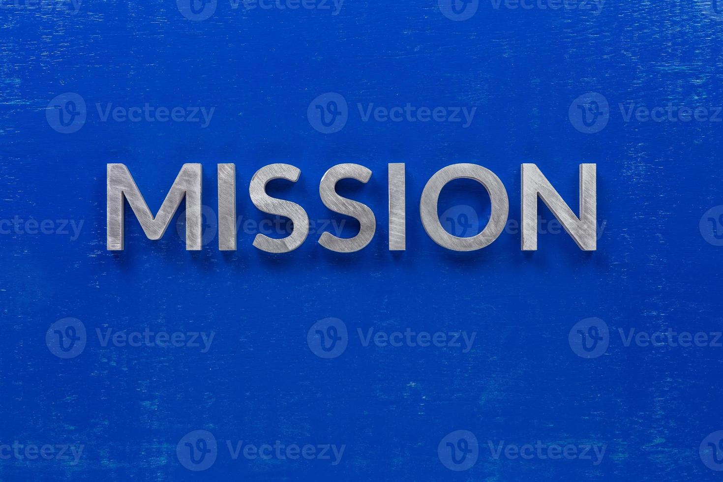 le mot mission posé avec des caractères en métal argenté sur une planche en bois peinte en bleu dans la composition centrale à plat photo