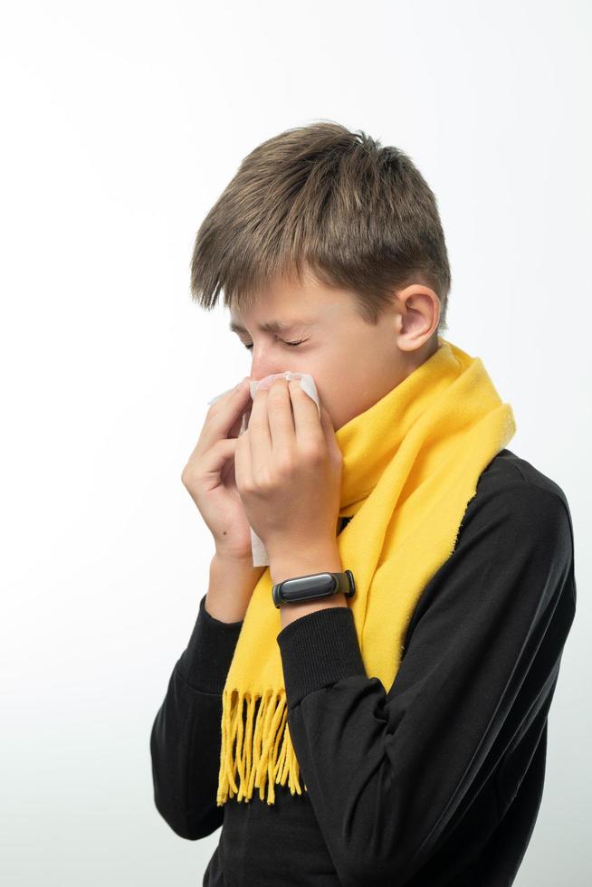 un garçon enveloppé dans une écharpe a le nez qui coule et se mouche dans une serviette. photo