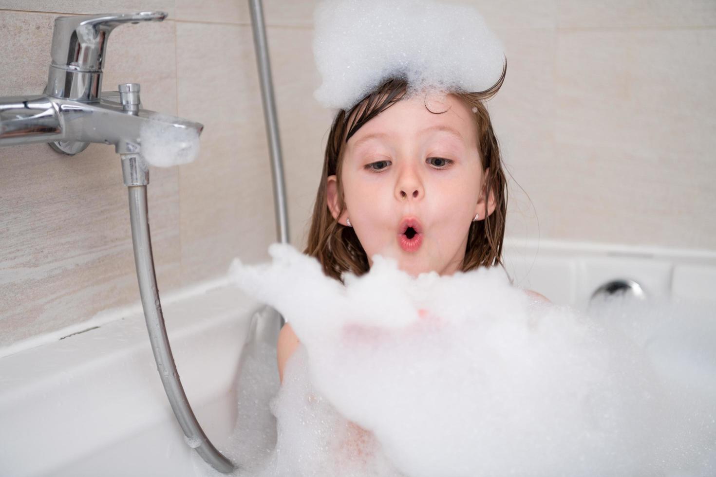 petite fille dans le bain jouant avec de la mousse photo