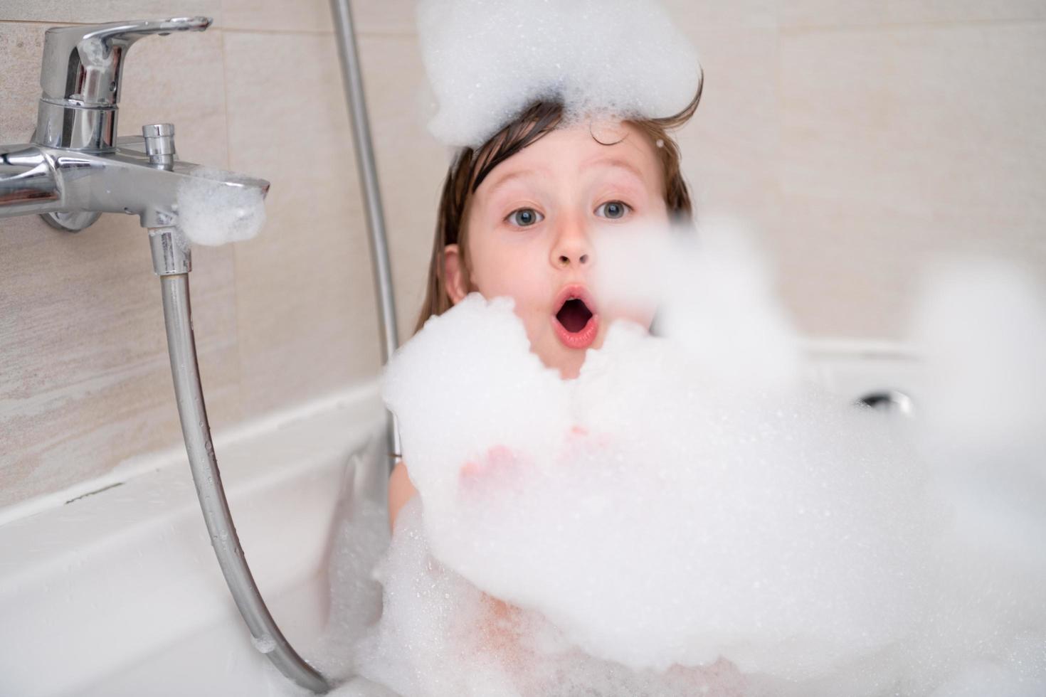 petite fille dans le bain jouant avec de la mousse photo