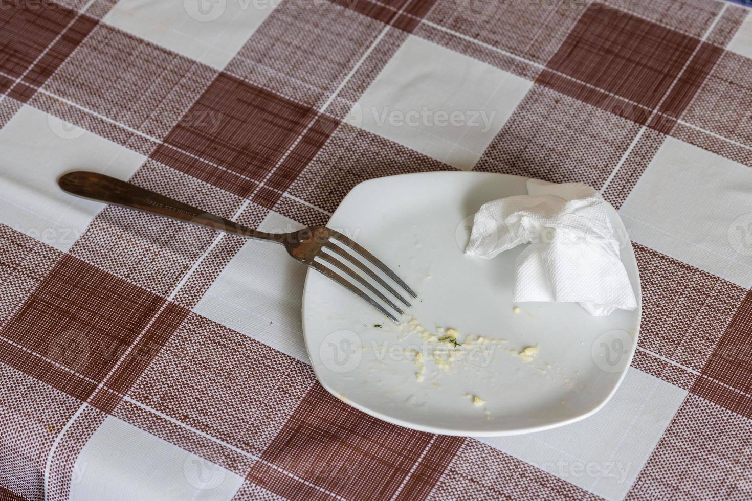 plat blanc vide avec des restes de nourriture mangée, une serviette de table froissée et une fourchette en acier photo
