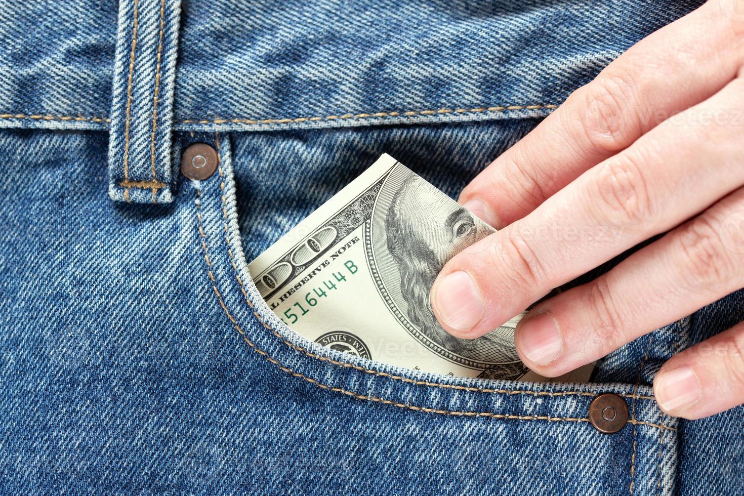 la main nous prend un billet en dollars de la poche avant droite du jean bleu. concept d'économiser de l'argent ou des dépenses de poche photo