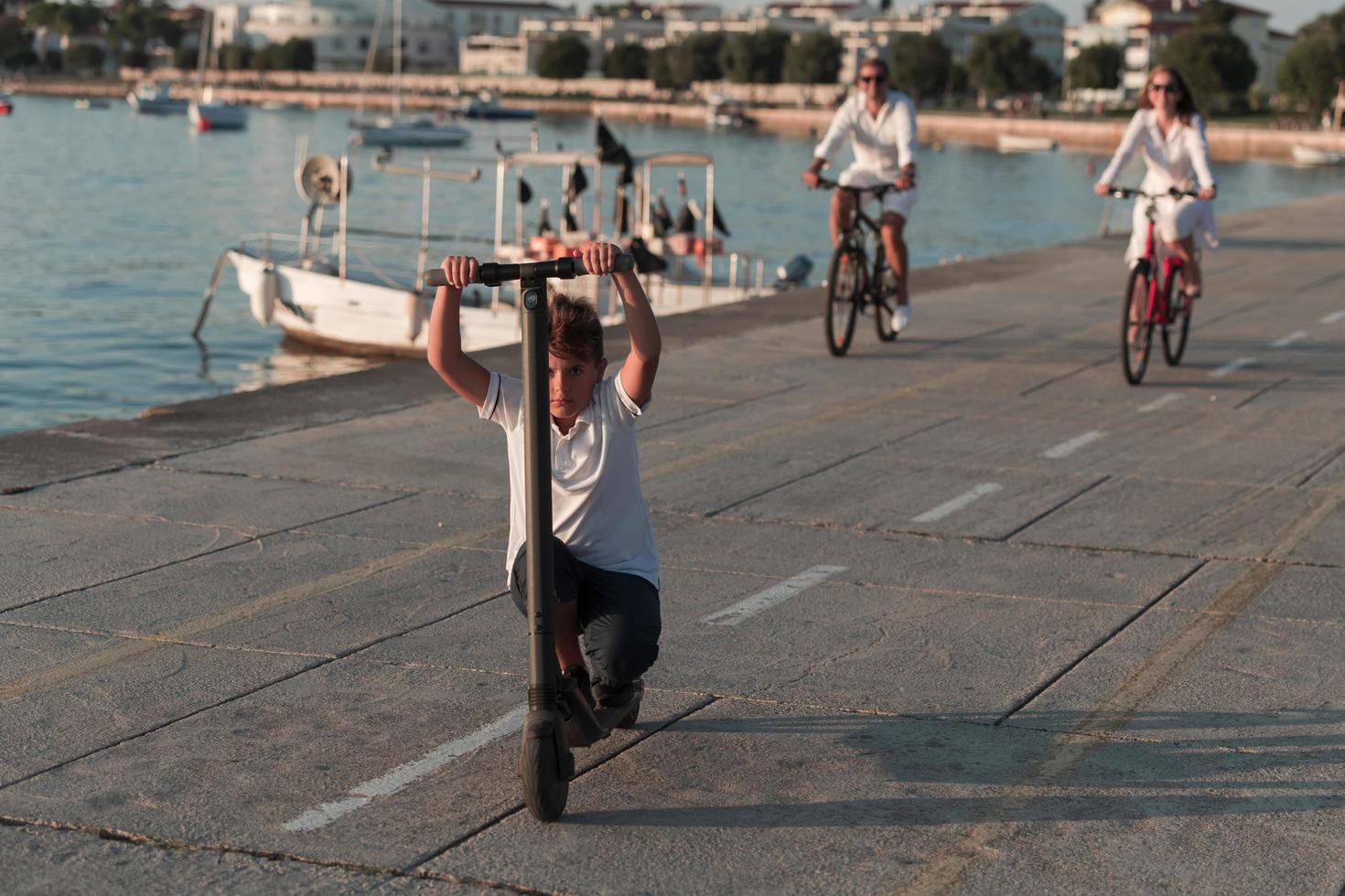 famille heureuse profitant d'une belle matinée au bord de la mer ensemble, parents faisant du vélo et leur fils faisant du scooter électrique. mise au point sélective photo