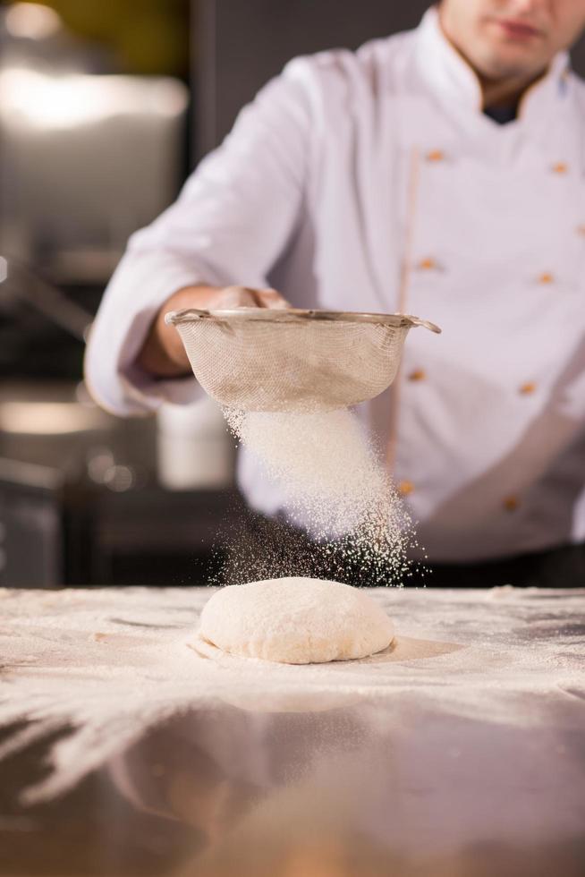 chef saupoudrant de farine sur la pâte à pizza fraîche photo