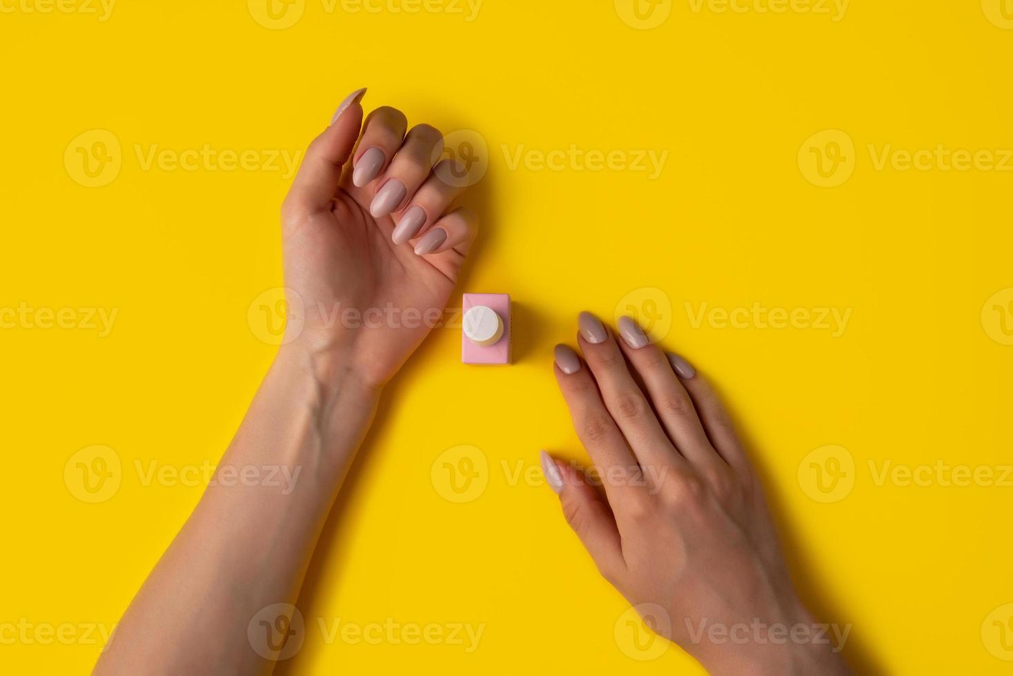 vernis gel de couleur rose et mains avec manucure sur fond jaune, vue de dessus photo