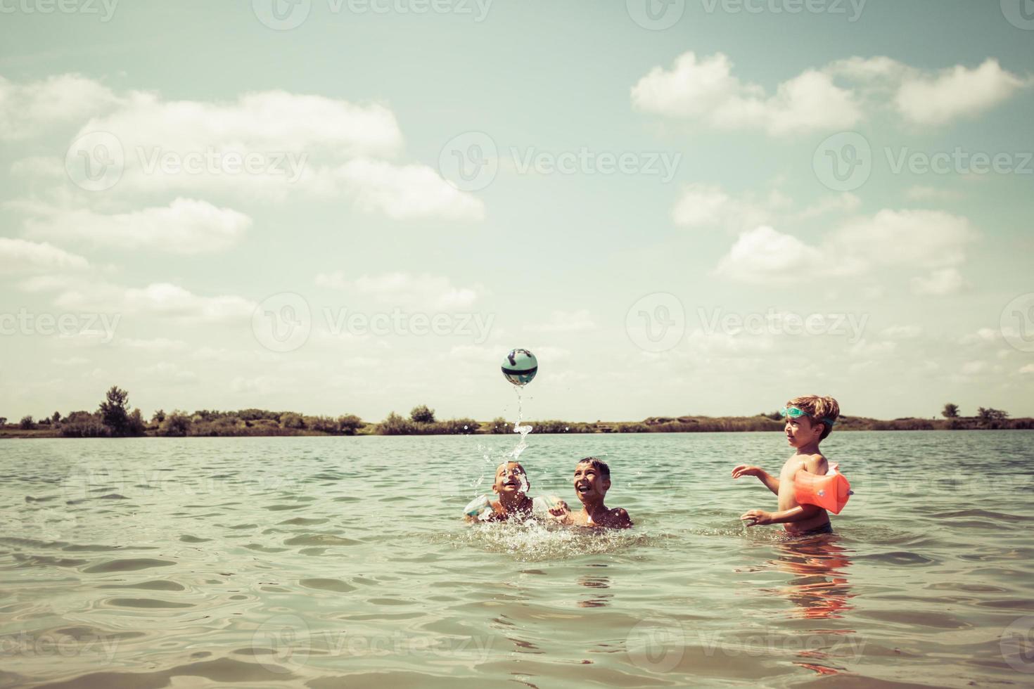 garçons heureux jouant avec le ballon dans l'eau pendant la journée d'été. photo