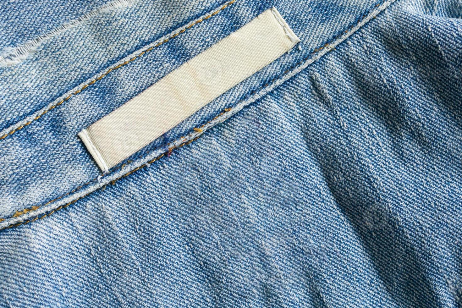 Étiquette de vêtements de soin de lessive blanche vierge sur fond de texture de jeans en denim photo