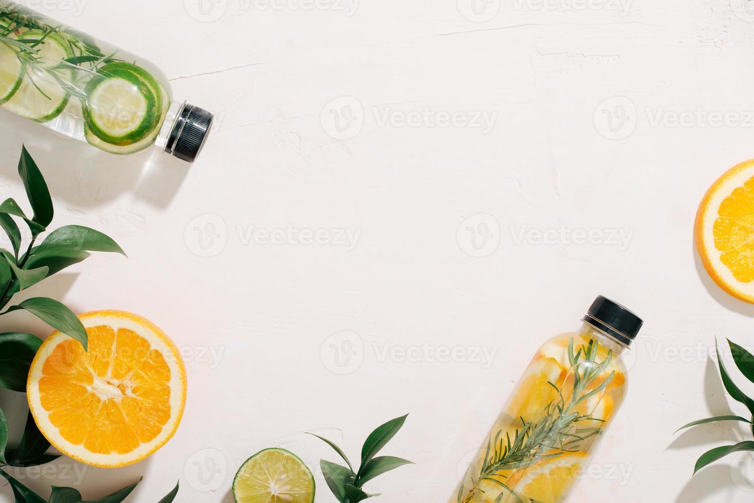 feuilles et bouteille d'eau tropicale sur fond blanc. eau infusée aux fruits détox, agrumes et feuilles de romarin. vue de dessus, mise à plat, espace de copie photo