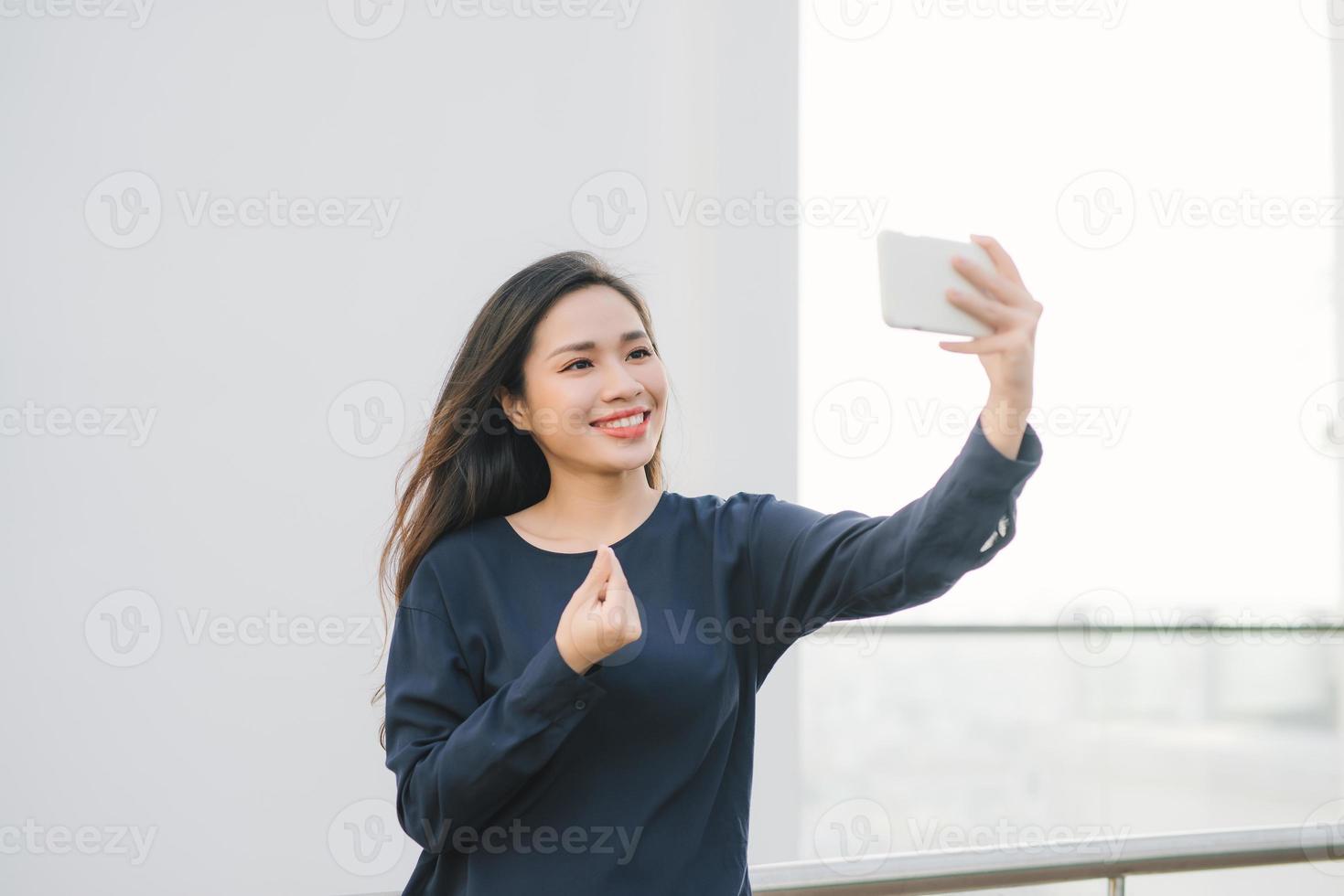 détendu et joyeux. travail et vacances. portrait extérieur d'une jeune femme heureuse utilisant un smartphone, faisant une photo de selfie et vous regardant sur la terrasse avec une belle vue sur la ville.