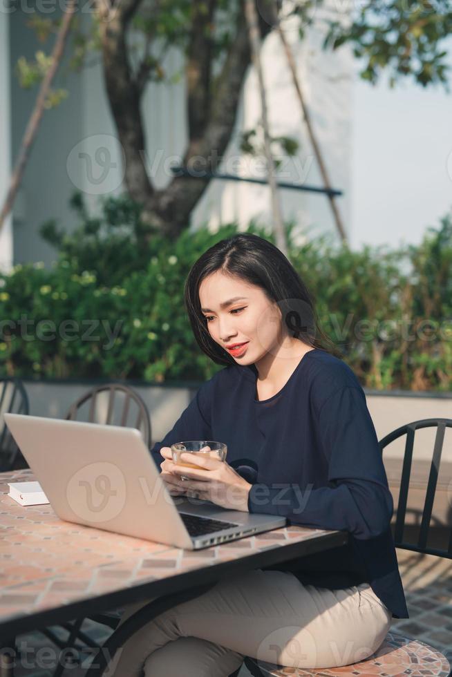 en profitant du wi-fi gratuit. belle jeune femme travaillant sur un ordinateur portable et souriant assis à l'extérieur photo