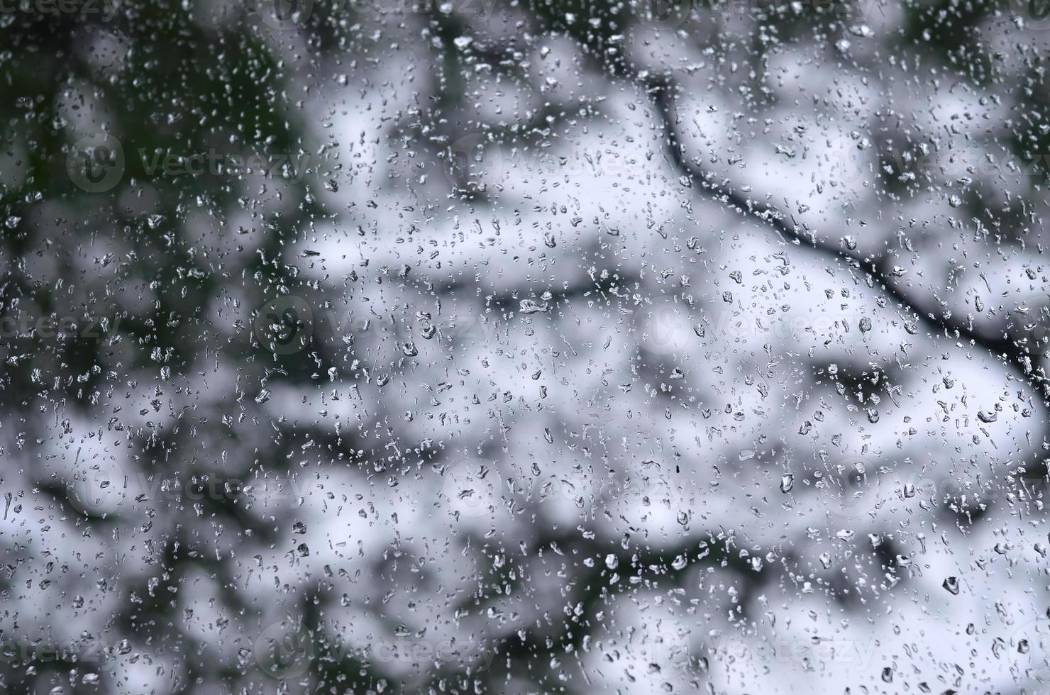 une photo de gouttes de pluie sur la vitre avec une vue floue des arbres verts en fleurs. image abstraite montrant des conditions météorologiques nuageuses et pluvieuses