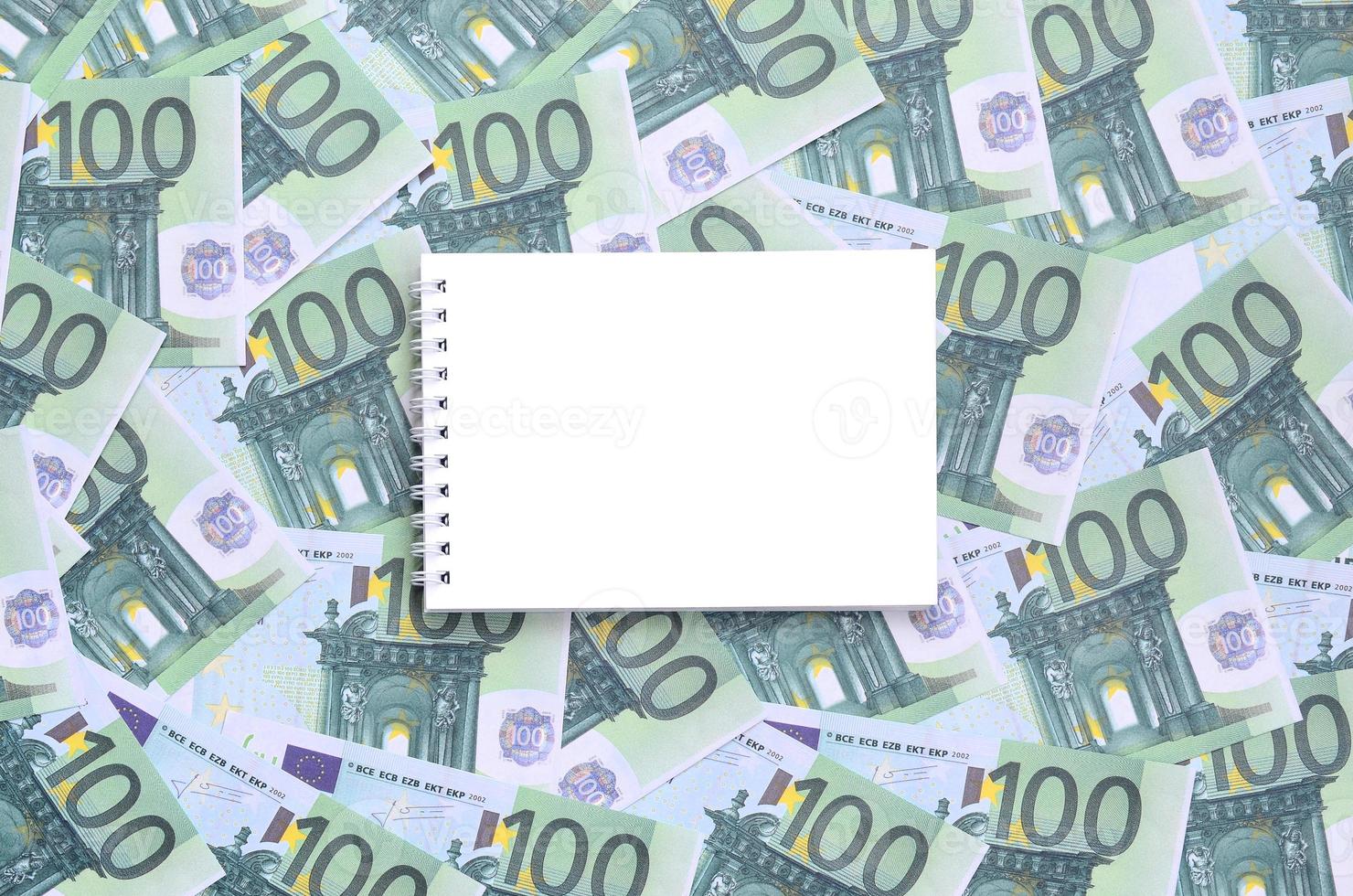 cahier blanc avec des pages propres se trouvant sur un ensemble de coupures monétaires vertes de 100 euros. beaucoup d'argent forme un tas infini photo