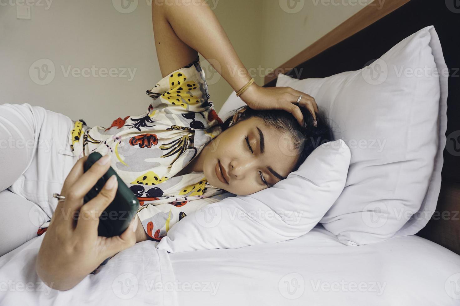 une jolie jeune femme s'endort en tenant son téléphone portable sur le lit. photo