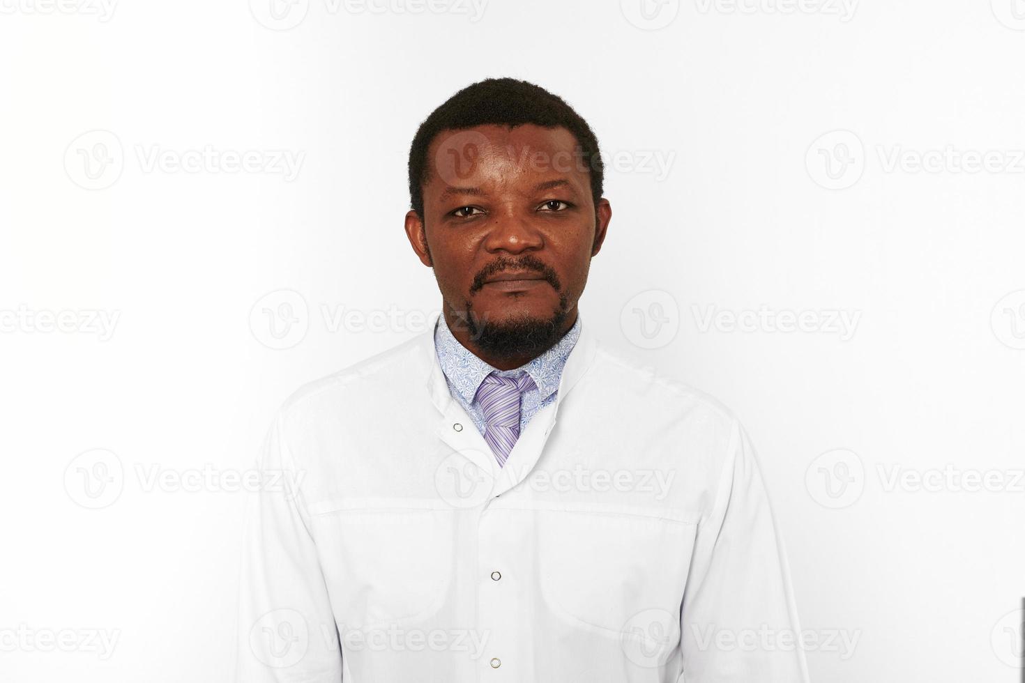 Homme médecin noir sérieux avec petite barbe en blouse blanche chemise lumineuse isolé sur fond blanc photo