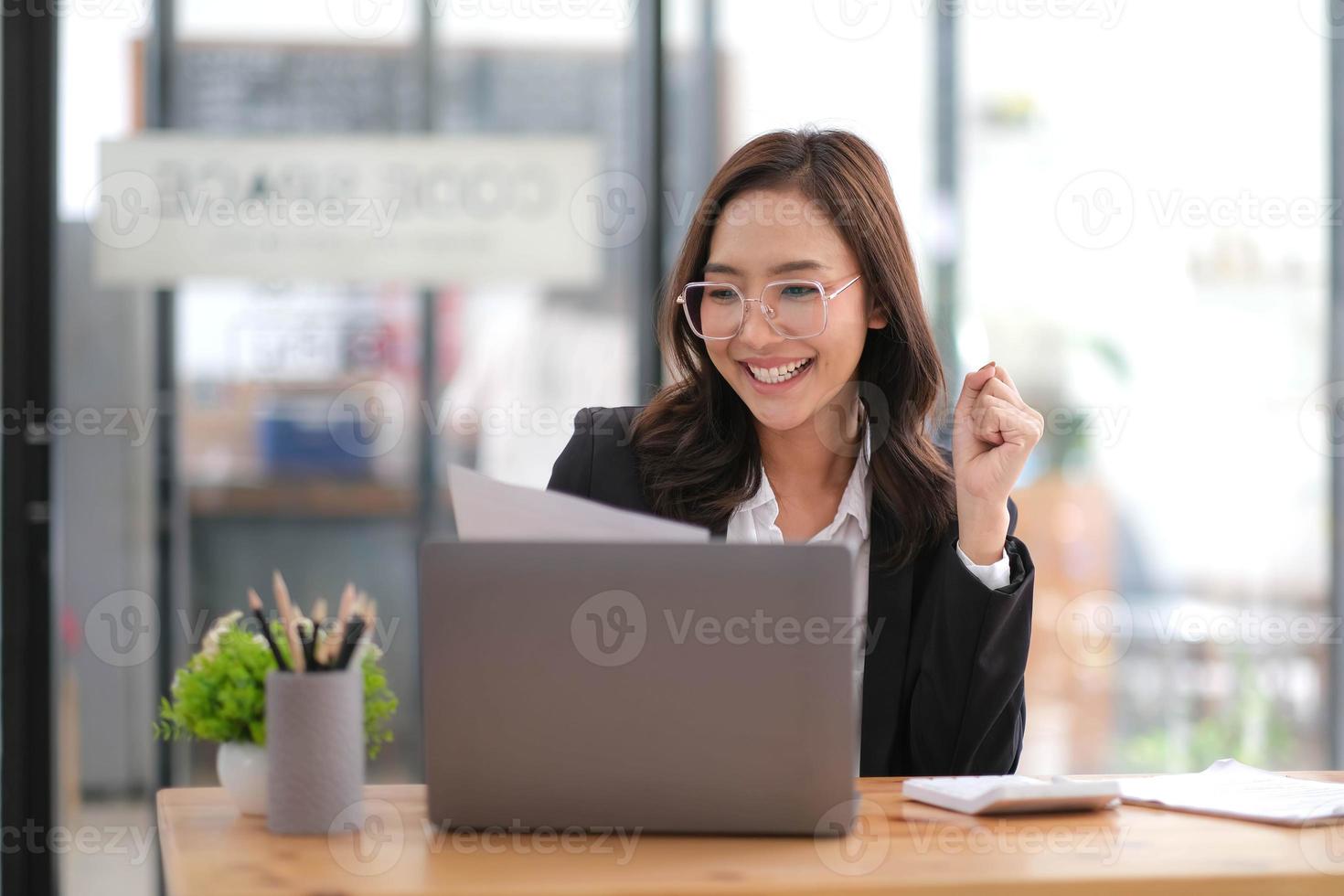 heureuse femme d'affaires asiatique réussie excitée triomphant avec un ordinateur portable et du papier dans le bureau de travail photo